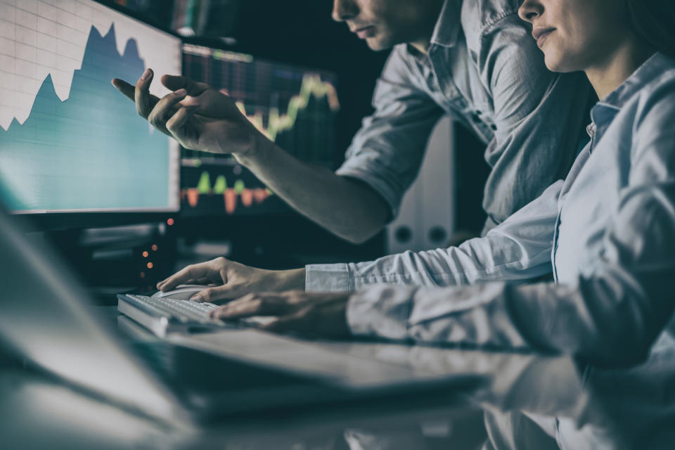 Two people looking at a computer screen with a stock chart on it.