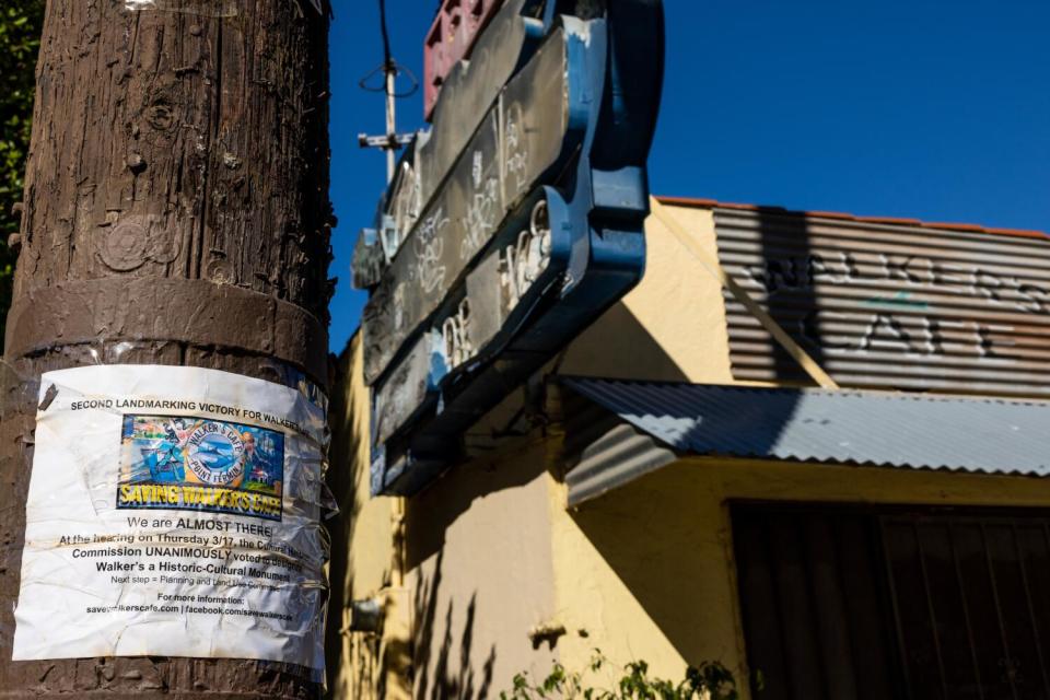 The damaged remnants of a neon blade sign outside an old, shuttered cafe building.