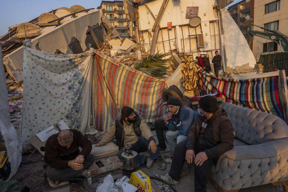 Men sit in front of the rubble of an area destroyed during the earthquake in Antakya, southeastern Turkey, Sunday, Feb. 12, 2023. Ever since the powerful 7.8 earthquake that has become Turkey's deadliest disaster in modern history, survivors have been gathering outside destroyed buildings, refusing to leave. (AP Photo/Bernat Armangue)
