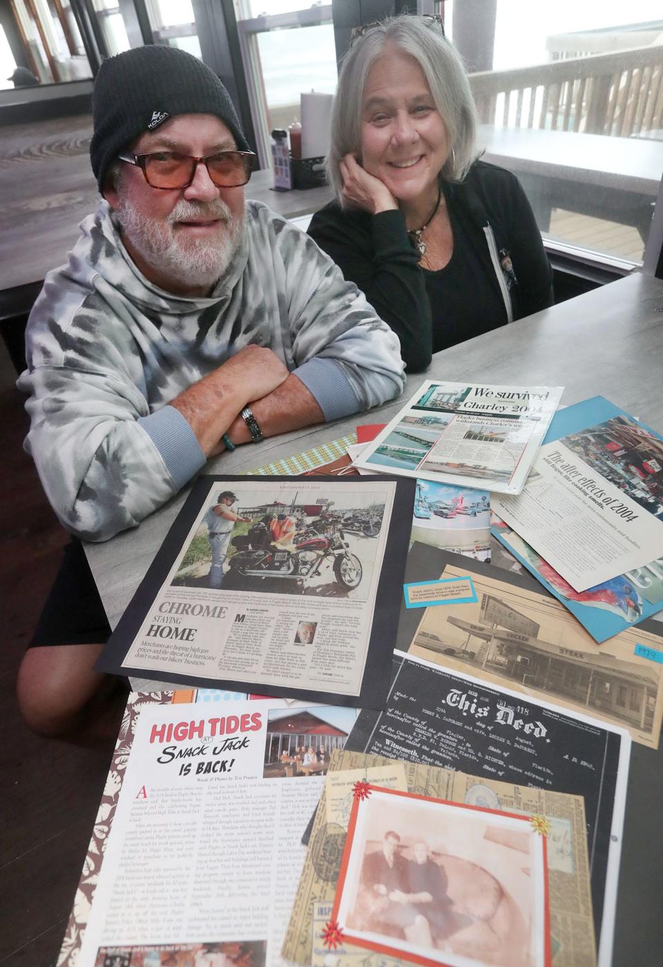 Ted Bancroft, general manager, and owner Gail Holt look at a collection of clippings and photographs that represent the long history of High Tides at Snack Jack in Flagler Beach. The restaurant has faced challenges from numerous hurricanes over the decades and is still going strong after nearly 80 years.