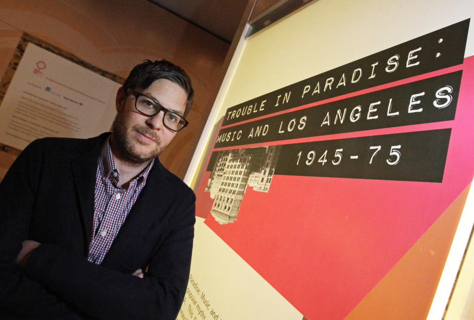 This March 26, 2012 photo shows Josh Kun, professor of Communications and Journalism at the University of Southern California, posing with the exhibit he curated, "Trouble In Paradise: Music and Los Angeles, 1945-1975," at the Grammy Museum in downtown Los Angeles. The museum website says the exhibit focuses on the "tensions between alluring myths of Southern California paradise and the realities of social struggle that characterized the years following WWII." (AP Photo/Reed Saxon)