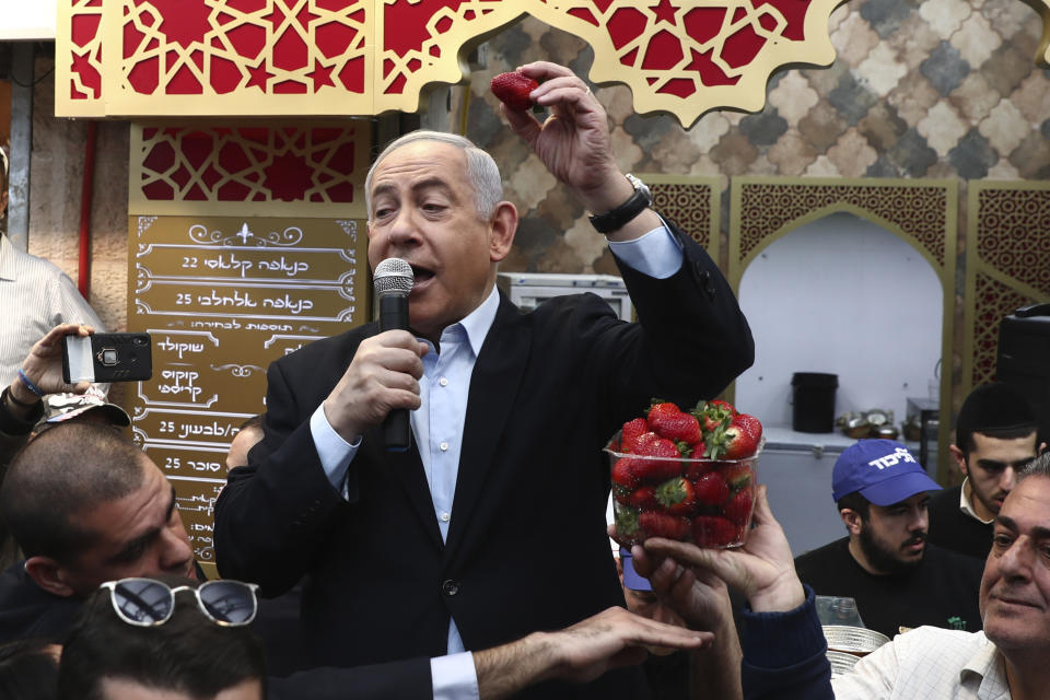 Israeli Prime Minister and head of the Likud party Benjamin Netanyahu holds a strawberry as he speaks during a visit to a market in Jerusalem, Friday, Feb. 28, 2020. (AP Photo/Oded Balilty)