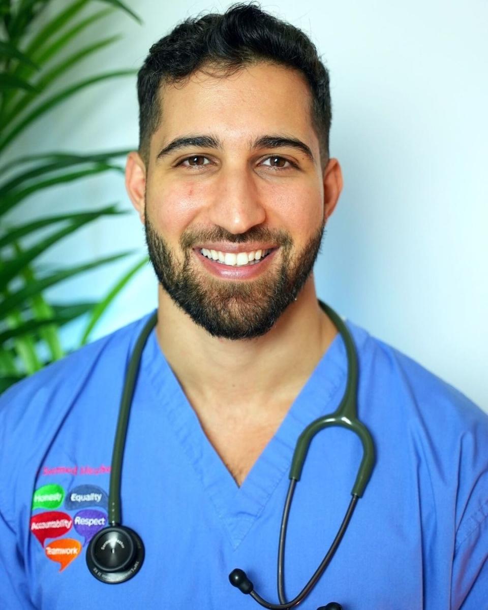 A smiling person in medical scrubs with a stethoscope around their neck. The scrubs have embroidered values like honesty, equality, and respect