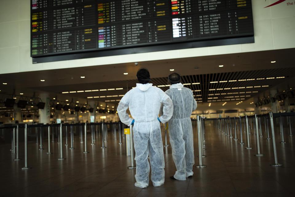 FILE - In this Wednesday, July 29, 2020 file photo, passengers, wearing full protective gear to protect against the spread of coronavirus, look at the departures board, at the Zaventem international airport in Brussels. The European Union's executive body proposed Monday Jan. 25, 2021, that the bloc's 27 nations impose more travel restrictions to counter the worrying spread of new coronavirus variants but make sure to keep goods and workers moving across EU borders. (AP Photo/Francisco Seco, File)