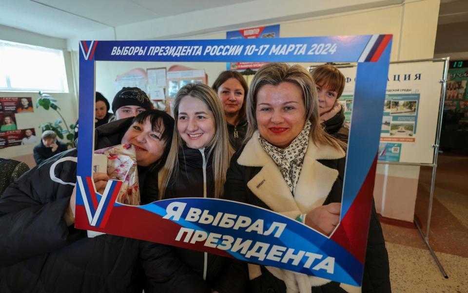 Voters pose with a frame reading 'I voted for the president' during the Russian presidential elections in Makeevka, Donetsk