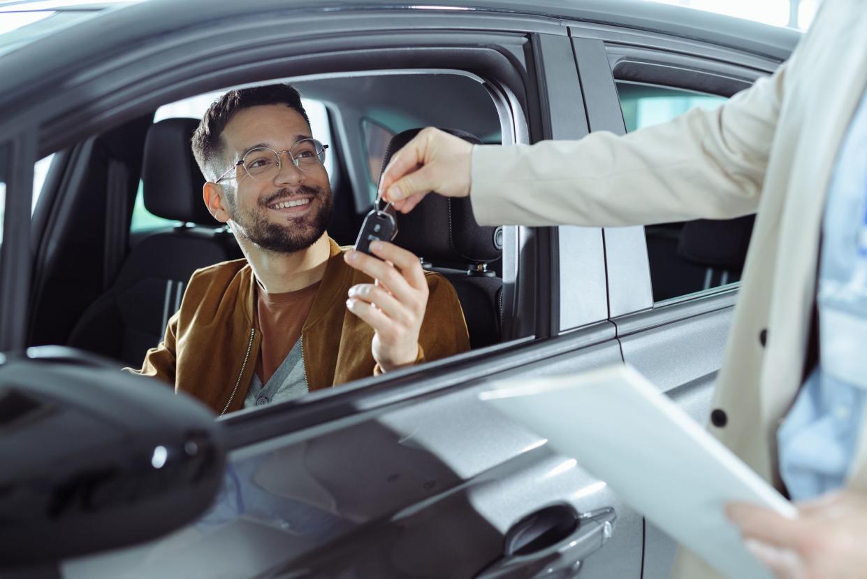 Happy man receiving keys for his new car in a showroom