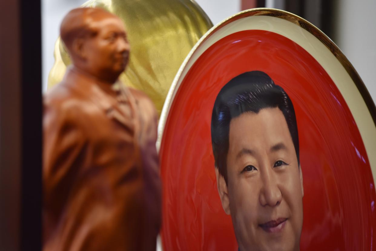 <p>A decorative plate featuring an image of Chinese President Xi Jinping is seen behind a statue of late communist leader Mao Zedong at a souvenir store next to Tiananmen Square in Beijing on 27 February, 2018</p> (GREG BAKER/AFP via Getty Images)