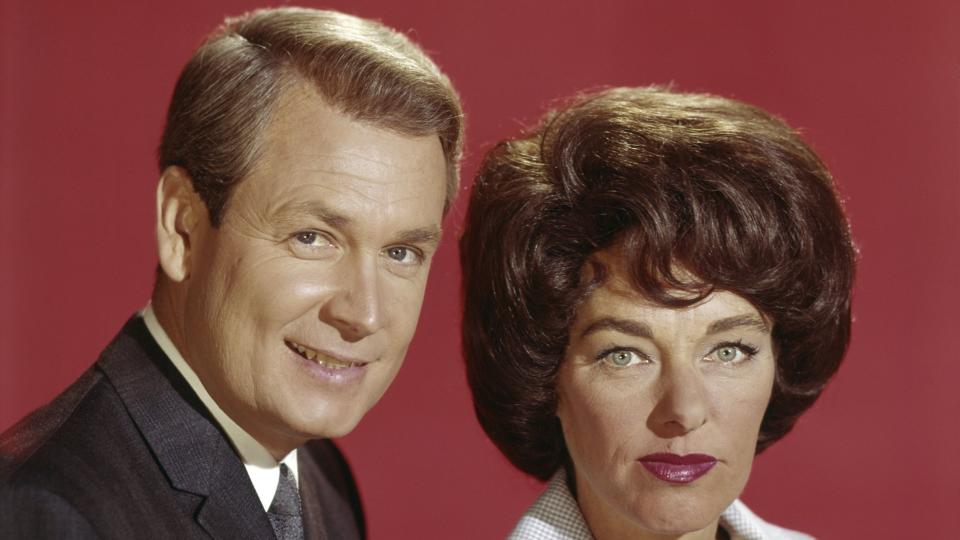 bob barker and dorothy jo gideon look directly at the camera, standing in front of a red wall