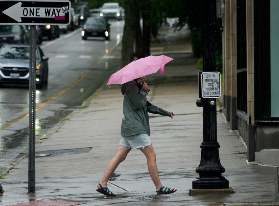 A woman with an umbrella walks along Providence's Thayer Street during a heavy rain in July.