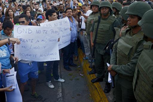 Manifestantes exhiben frente a efectivos de la Guardia Nacional Bolivariana (GNB) letreros que dicen "GNB no te pares frente a mi, párate a mi lado y sacúdete (golpea) al cubano" en la plaza de Altamira, Caracas, donde la oposición realiza sus principales movilizaciones, el 17 de marzo de 2014. (AFP | Leo Ramírez)