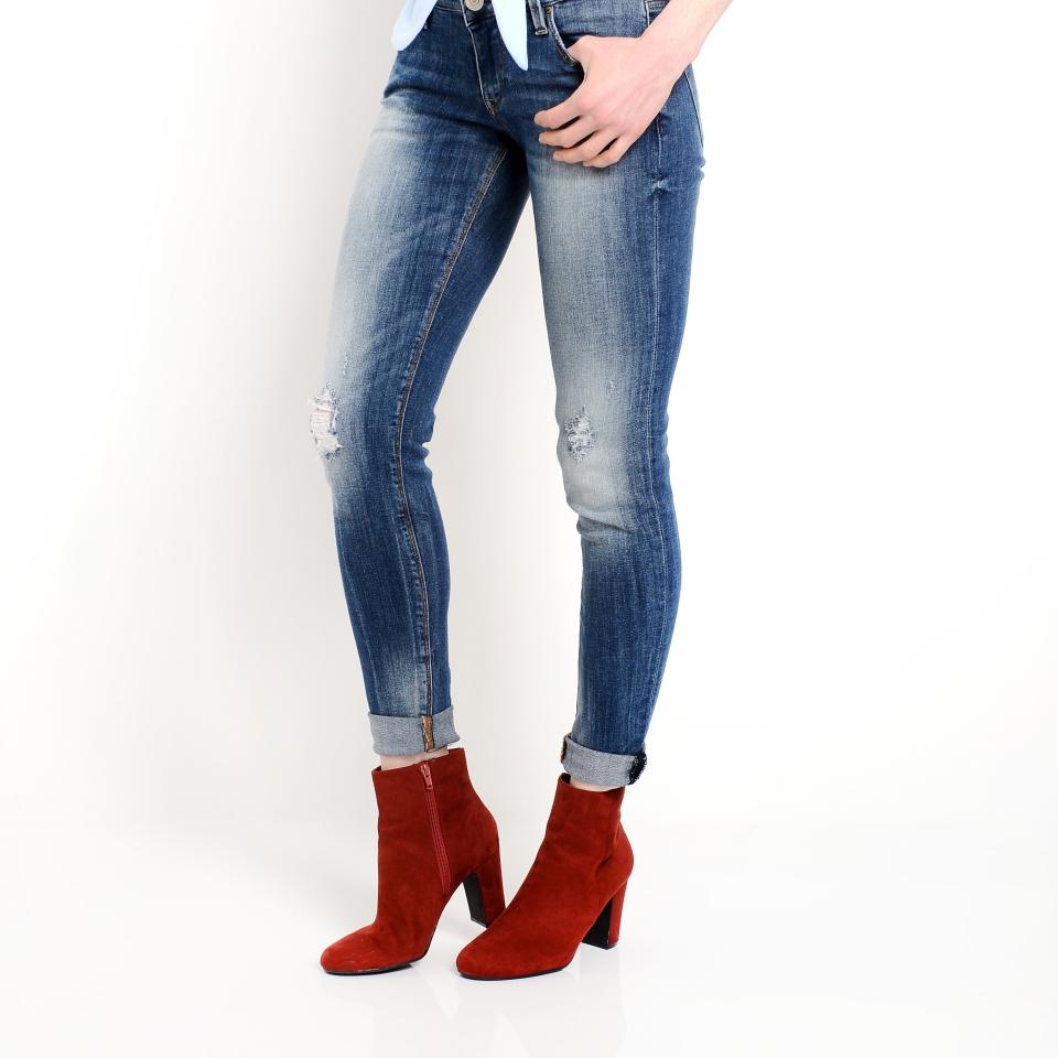 A person stands facing forward, wearing fitted, ripped jeans rolled at the ankles, a tied shirt, and red ankle boots