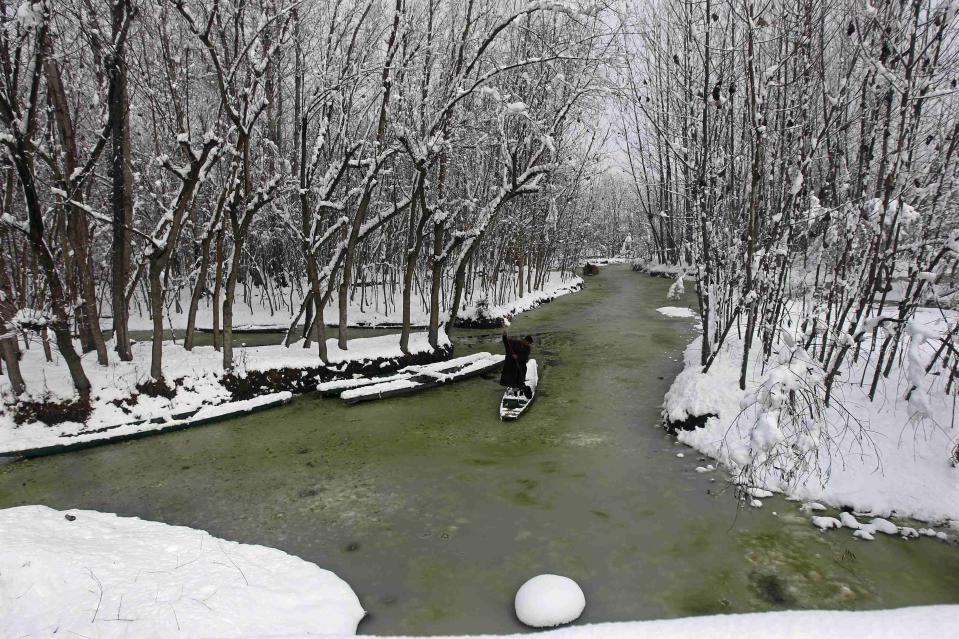 A Kashmiri man rows a boat through the waters of Anchar Lake after heavy snowfall in Srinagar