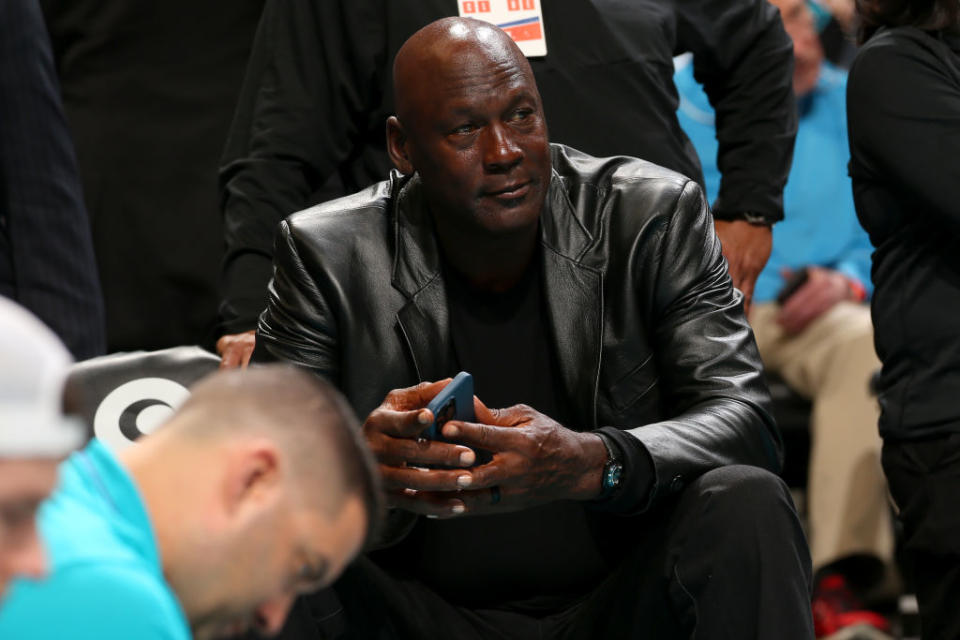 Close-up of Michael seated, holding a phone, and wearing a leather jacket