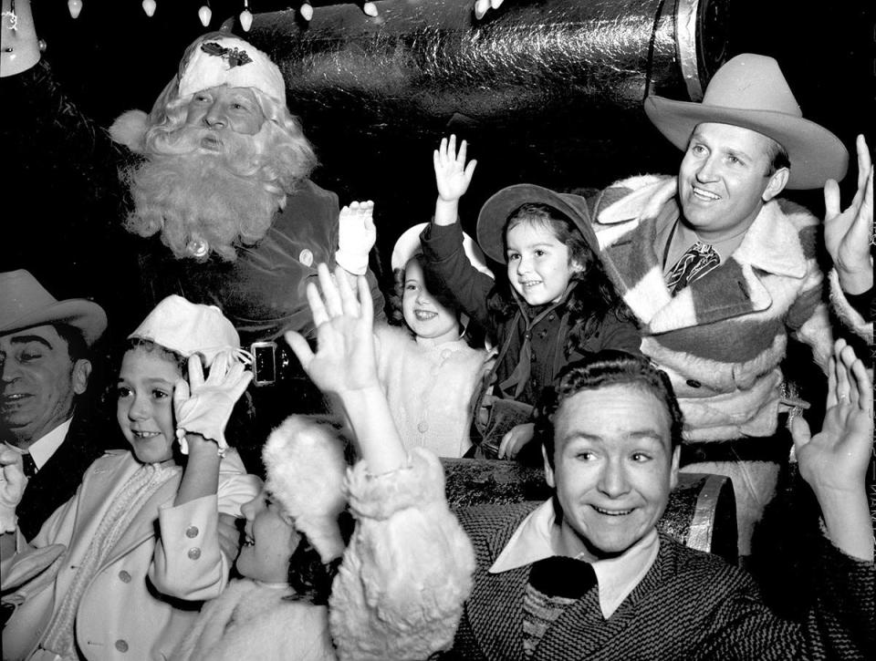 "Singing Cowboy" Gene Autry and eager fans join Santa Claus in waving to the crowd at a Christmas parade, circa 1940.