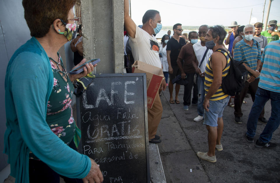 Residents wait in line to buy groceries next door to a coffee shop that has a sign announcing free coffee and water for those working to extinguish a deadly fire at a large oil storage facility in Matanzas, Cuba, Tuesday, Aug. 9, 2022. The fire was triggered by lighting that struck one of the facility’s eight tanks late Friday, Aug. 5th. (AP Photo/Ismael Francisco)