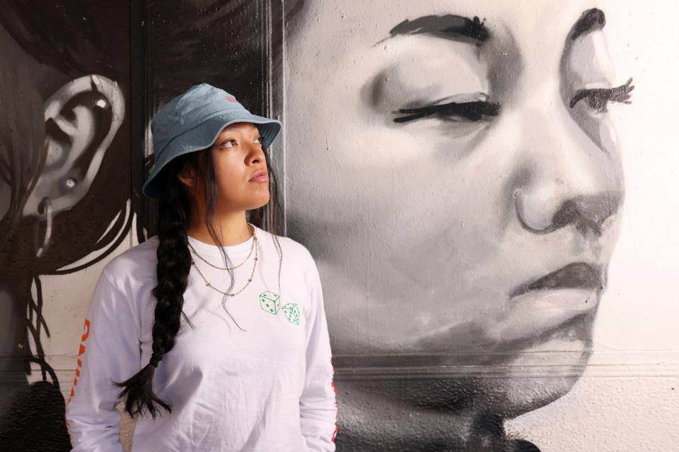 Alepsis Hernandez in front of her first paid commission, a mural showing a woman's face.