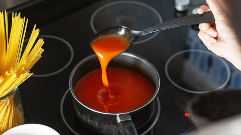 Hand spooning thick sauce in a pot on a stovetop