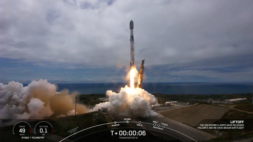 black-and-white spacex rocket launches into a foggy sky from a seaside launch pad