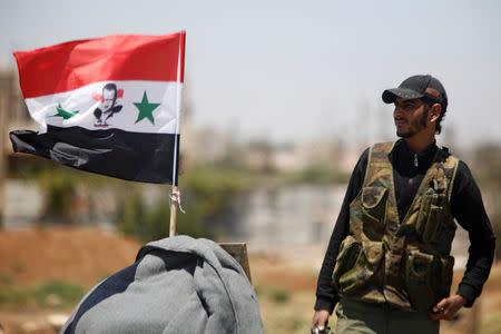 FILE PHOTO: A Syrian army soldier stands next to a Syrian flag in Umm al-Mayazen, in the countryside near Deraa, Syria, July 10, 2018. REUTERS/Omar Sanadiki/File Photo