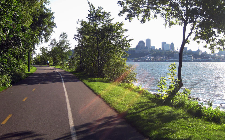 In this Aug. 17, 2013 photo, a cyclist rides along the St. Lawrence River across from Quebec City on an off-road trail in Levis. The trail offers a dedicated lane for walkers and two lanes for cyclists, and is part of the Route Verte bicycle network. (AP Photo/Calvin Woodward)