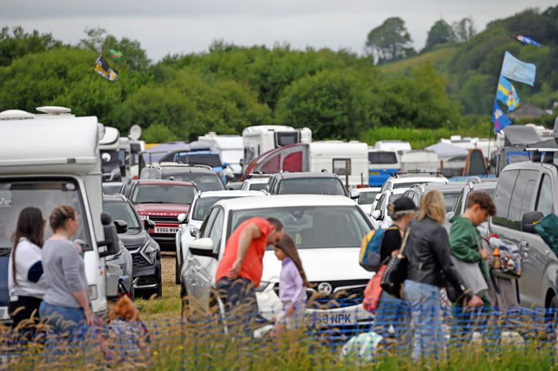 People walk past field of parked cars