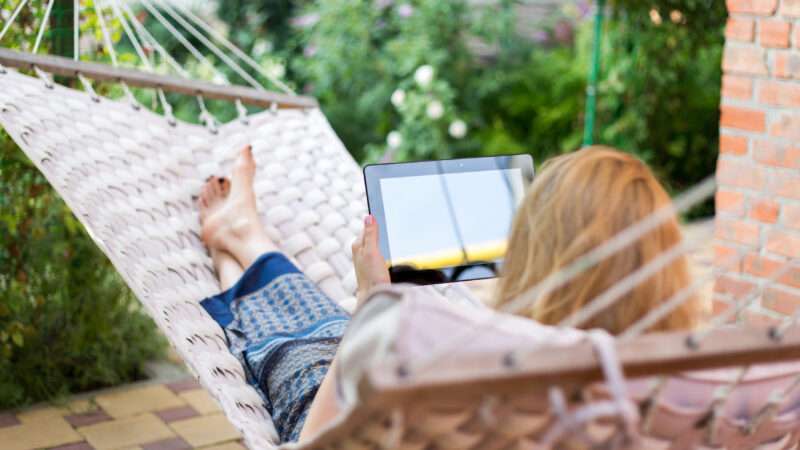 Someone relaxes in a hammock while holding a tablet
