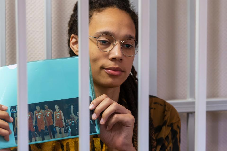 Brittney Griner holds up a photo of players from the recent WNBA All-Star Game wearing her number while sitting in a cage in a Russian court room.