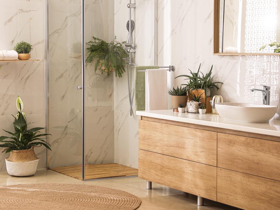 A bathroom with white tile, wooden detail, and several plants