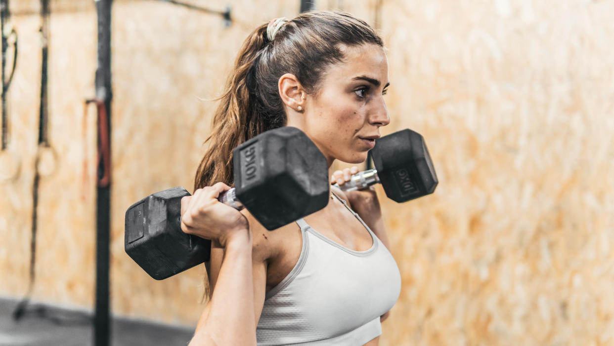  Woman in gym holds dumbbells by her shoulders. 