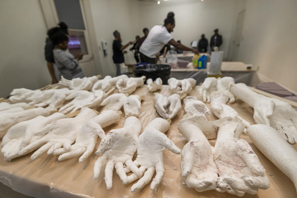 Cast hands made from local volunteers are displayed on a table in Charleston, S.C., Saturday, Feb. 18, 2023. Artist Stephen Hayes, background center, will use the molds to make a memorial for 36 enslaved people whose bodies were unearthed in Charleston in 2013 during a construction project for the Gaillard Center. (AP Photo/Mic Smith)