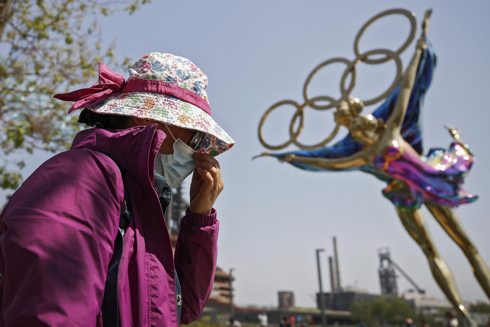 FILE - In this May 2, 2021, file photo, a woman adjusts her face mask as she walks by a statue featuring the Beijing Winter Olympics figure skating on display at the Shougang Park in Beijing. China's "zero tolerance" strategy of trying to isolate every case and stop transmission of the coronavirus has kept kept the country where the virus first was detected in late 2019 largely free of the disease. (AP Photo/Andy Wong, File)