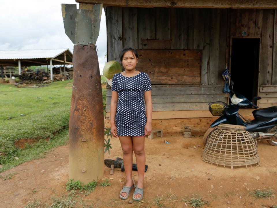 A girl poses at an entrance of her house next to a bomb dropped by the U.S. Air Force planes during the Vietnam War, in the village of Ban Napia in Xieng Khouang province, Laos