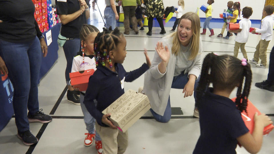 A volunteer waves to a student as she waits in line at Miles Intermediate Elementary School in Atlanta after receiving new shoes from Mercedes-Benz USA, as a part of their Season to Shine holiday program, on Wednesday, Dec. 7, 2022. (AP Photo/Sharon Johnson)