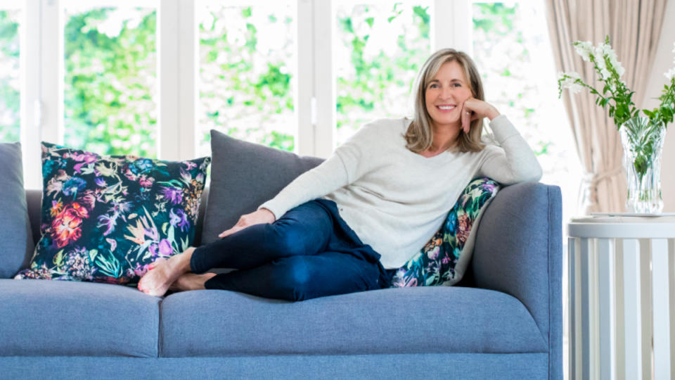 A woman sitting on a dark blue couch resting her head on her hands after enjoying the benefits of beetroot for females