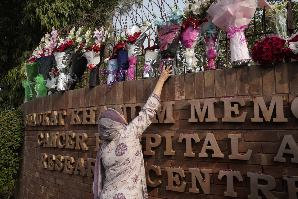 A woman places bouquet over the wall of a hospital where former Pakistani Prime Minister Imran Khan is being treated for a gunshot wound in Lahore, Pakistan, Friday, Nov. 4, 2022. Khan who narrowly escaped an assassination attempt on his life the previous day when a gunman fired multiple shots and wounded him in the leg, is listed in stable condition after undergoing surgery at a hospital, a senior leader from his party said Friday. (AP Photo/K.M. Chaudhry)