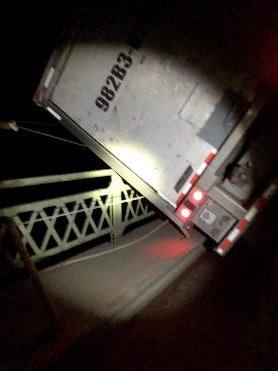 In this Wednesday, Jan. 13, 2021, photo provided by the Washington State Department of Transportation, a tractor-trailer leans against bridge railing where it blew over amid heavy wind gusts as it attempted to travel over the Deception Pass Bridge north of Seattle. Part of the truck was left dangling over the edge of the bridge, but the driver escaped unharmed. (Washington State Department of Transportation via AP)