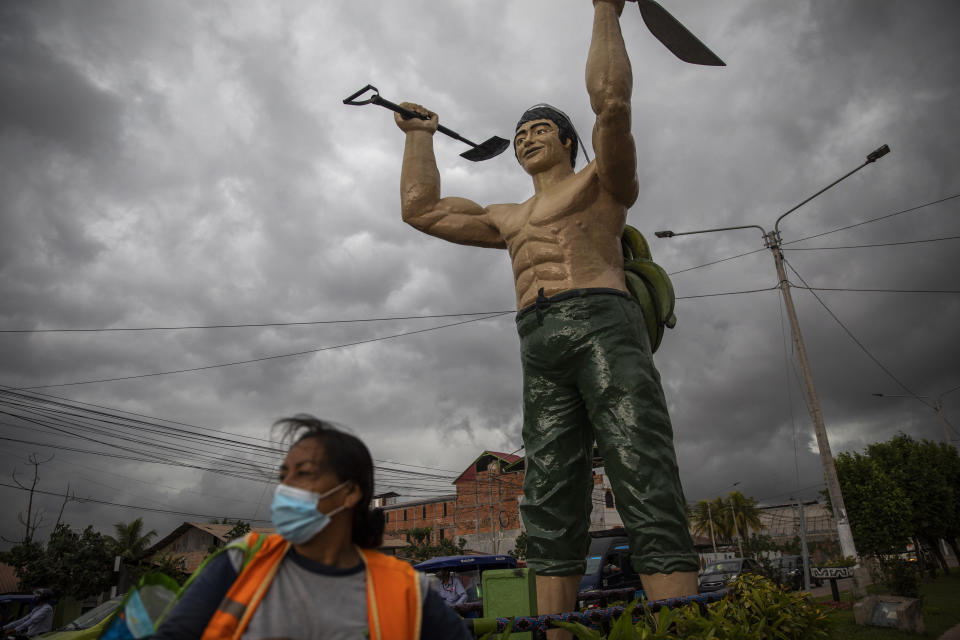 A woman using a protective face mask amid the new cornavirus pandemic, stands next to the monument "El hombre Chacarero," that represents a rural worker, in Pucallpa, Peru's Ucayali region, Monday, Sept. 28, 2020. The Ucayali region located along a muddy river has long seen periodic dengue outbreaks, but this year’s figures are already three times that seen in 2019. (AP Photo/Rodrigo Abd)