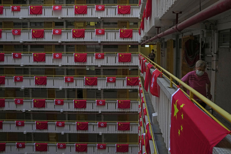 A resident walks besides the Chinese and Hong Kong flags hanging from a residential building to celebrate the 25th anniversary of Hong Kong handover to China, at a public housing estate, in Hong Kong, Saturday, June 25, 2022. As the former British colony marks the 25th anniversary of its return to China, reeling from pandemic curbs that devastated business and a crackdown on its pro-democracy movement, Hong Kong leaders say it is time to transform again and become a tech center that relies more on ties with nearby Chinese factory cities than on global trade. (AP Photo/Kin Cheung)