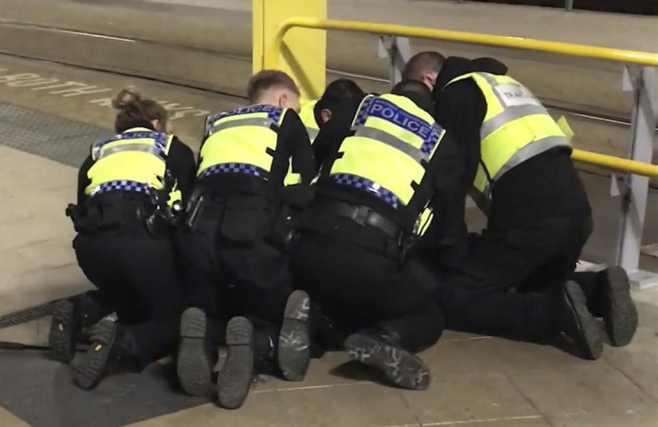 UGC issued by PA shows Police restraining a man after he stabbed three people at Victoria Station in Manchester, England, late Monday Dec. 31, 2018. Two commuters - a man and woman in their 50s - were taken to hospital with knife injuries and a British Transport Police (BTP) officer was stabbed in the shoulder. Police said a man was arrested on suspicion of attempted murder and remains in custody. (Sam Clack/PA via AP)