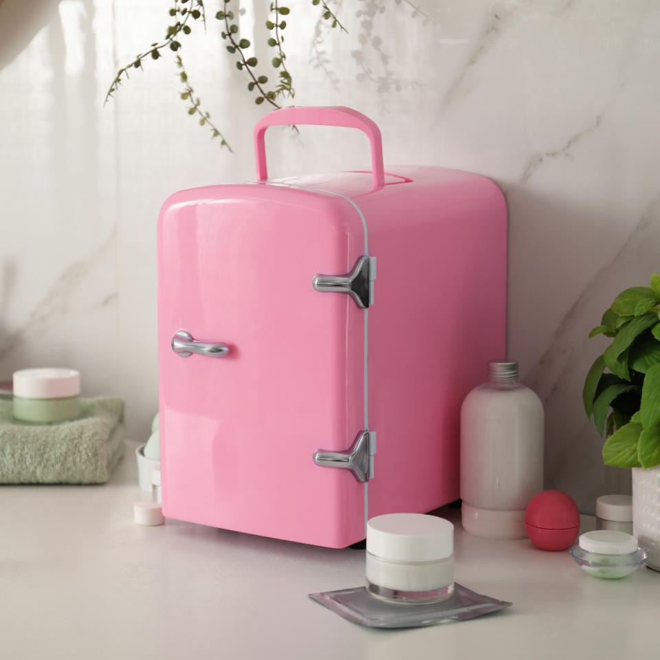 Pink mini fridge on countertop next to skincare products