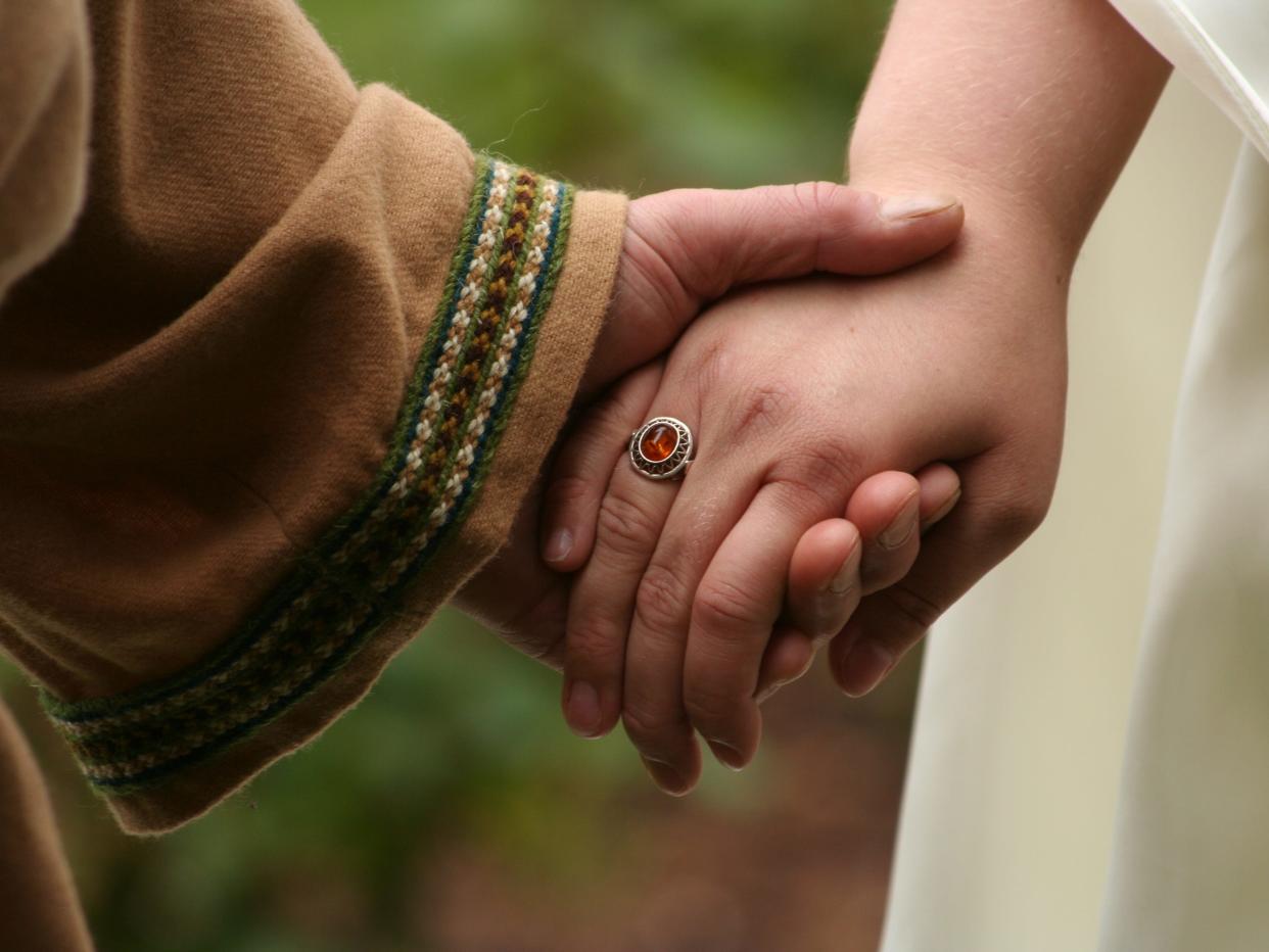 Two hands holding each other, one is wearing a gold ring with a red gem