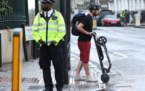 An e-scooter rider pushes his e-scooter after being stopped by a police officer in Islington - Credit: Yui Monk/PA
