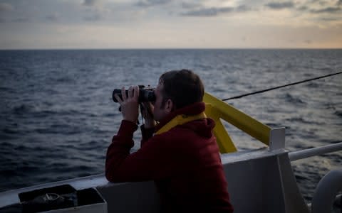 One of the crew members of the Dutch-flagged rescue vessel Sea Watch 3 keeps a watch on the sea with binoculars on January 18, 2019 during a rescue operation off Libya's coasts - Credit: FEDERICO SCOPPA/AFP