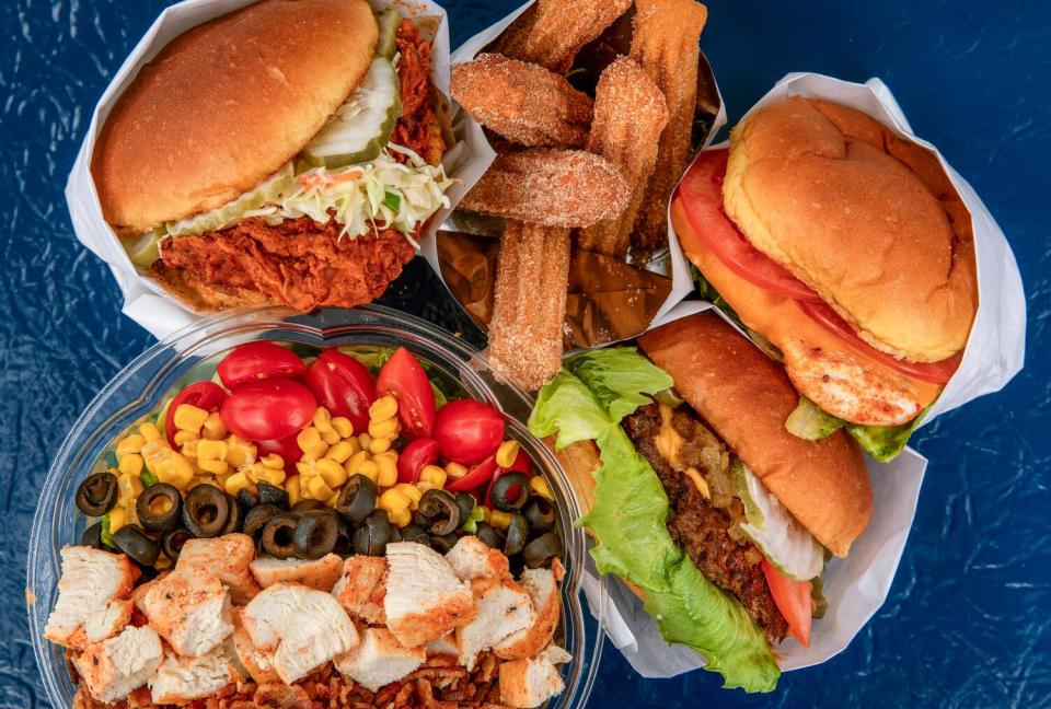 An array of sandwiches, salad and churros on a dark blue surface.