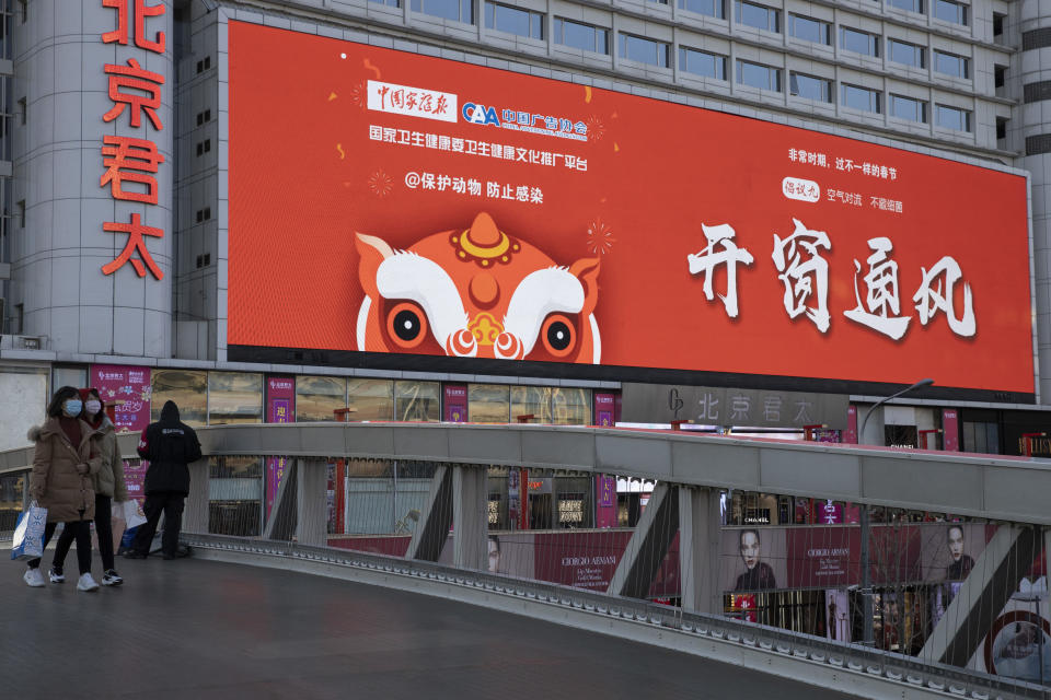 In this photo taken Saturday, Feb. 22, 2020, shoppers walk near a mall display with the government slogan "Open windows and allow air to flow" in Beijing, China. Regulators on Monday promised tax cuts and other aid to help companies recover from China's virus outbreak and expressed confidence the ruling Communist Party's growth targets can be achieved despite anti-disease controls that shut down much of the economy. (AP Photo/Ng Han Guan)