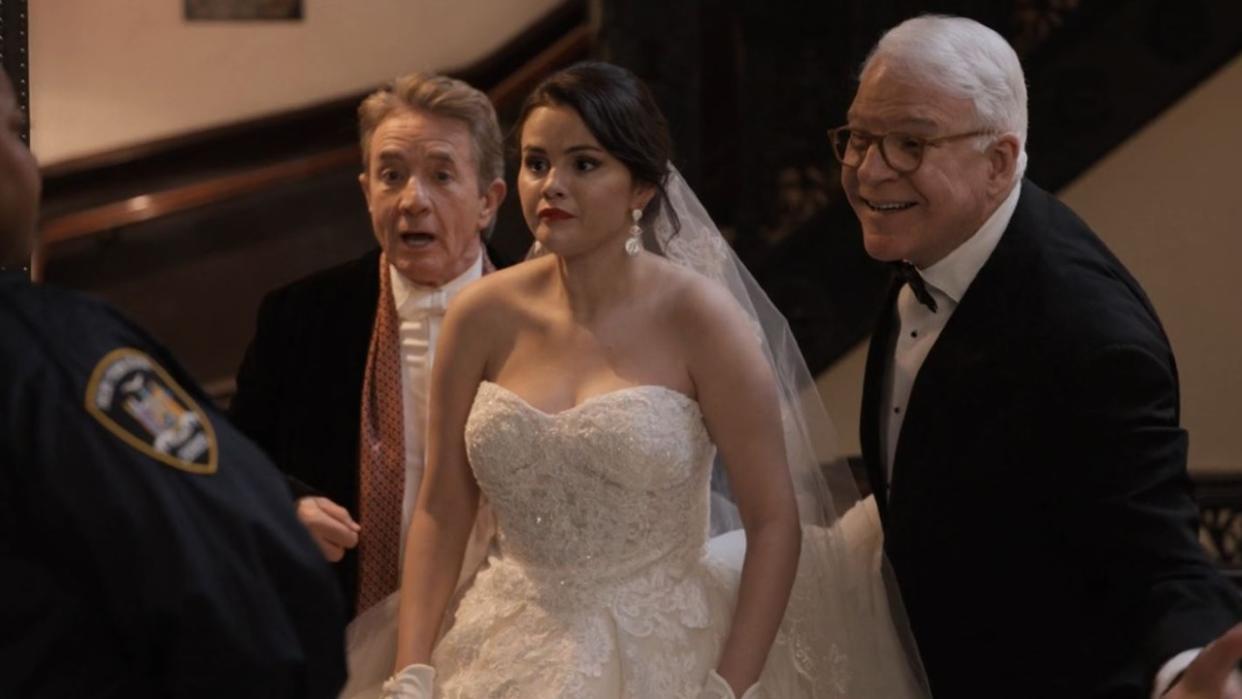  A screenshot from Only Murders in the Building of Selena Gomez in a wedding dress, with Steve Martin to the right of her smiling and Martin Short behind her looking a bit shocked. . 