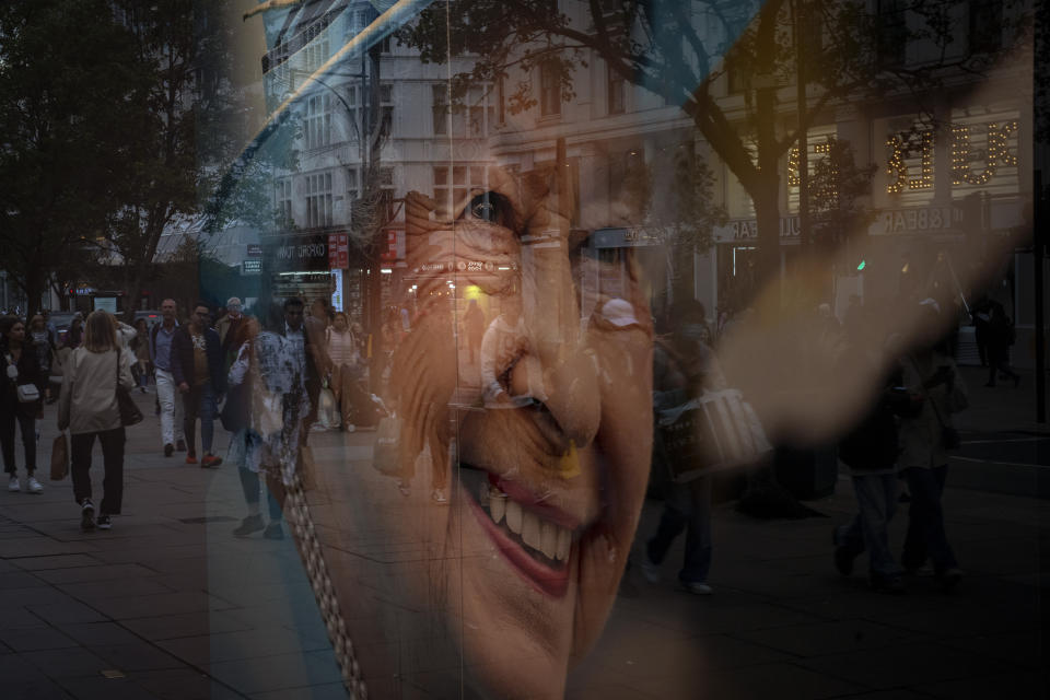 Pedestrians are seen reflected in the glass of a store displaying a portrait of the late Queen Elizabeth II in London, Thursday, Sept. 15, 2022. The Queen will lie in state in Westminster Hall for four full days before her funeral on Monday Sept. 19. (AP Photo/Emilio Morenatti)