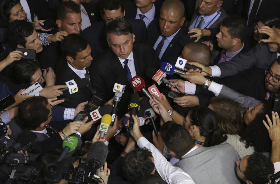 FILE - In this May 7, 2019 file photo, the press surrounds Brazil's President Jair Bolsonaro after he signed a second decree that eases gun restrictions at Planalto presidential palace in Brasilia, Brazil. Bolsonaro repeated a debunked sexually charged allegation about one of the country’s more prominent journalists on Tuesday, Feb. 18, 2020, drawing fire from press freedom advocates. (AP Photo/Eraldo Peres, File)