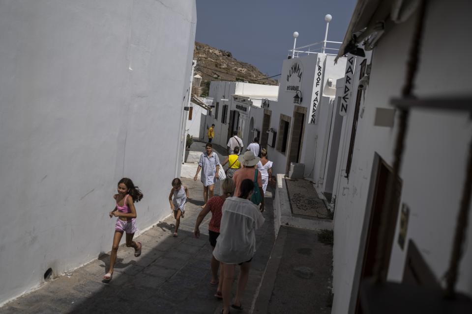 Tourists walk in Lindos, on the Aegean Sea island of Rhodes, southeastern Greece, on Thursday, July 27, 2023. The wildfires have raged across parts of the country during three successive Mediterranean heat waves over two weeks, leaving five people dead. (AP Photo/Petros Giannakouris)