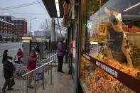 A worker hangs up a price tag for oranges as residents wearing masks line up to enter the supermarket which is controlling the numbers of shoppers in Beijing, China on Tuesday, Feb. 25, 2020. The new virus took aim at a broadening swath of the globe Monday, with officials in Europe and the Middle East scrambling to limit the spread of an outbreak that showed signs of stabilizing at its Chinese epicenter but posed new threats far beyond. (AP Photo/Ng Han Guan)